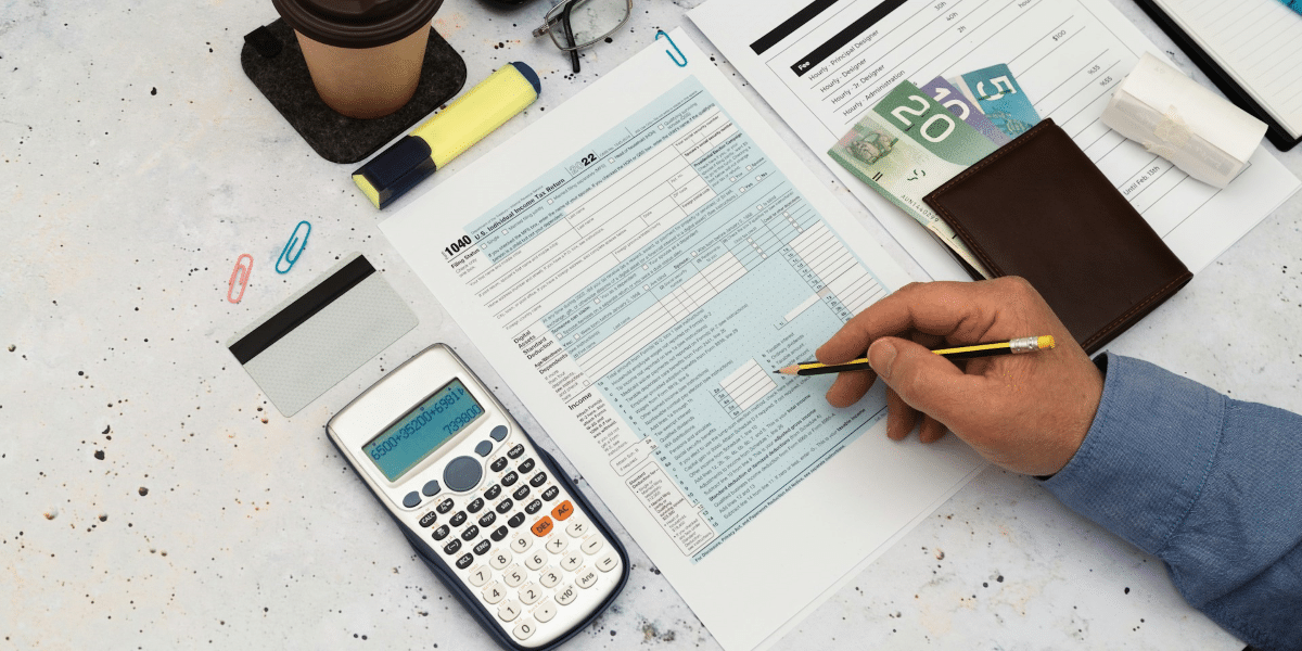 An individual calculating finances with a tax form, a calculator, and various financial documents spread out on a marble surface, symbolizing the thorough financial analysis and planning services provided by National Debt Relief. The scene represents a strategic approach to debt management and financial stability, emphasizing the importance of detailed planning and expert advice in overcoming financial challenges and achieving debt relief.